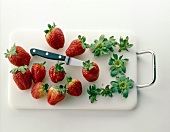 Fresh strawberries' leaves being removed with knife on cutting board