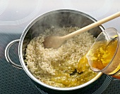 Broth being poured in rice and onions in pot