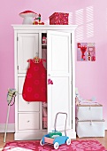 White wardrobe with red dress hanging against pink background