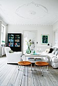 White living room with black cabinet, loose-covered armchair and leather stools
