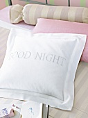 Kissen in Weiß mit Aufschrift "Good Night" auf Bett, andere Kissen rosa