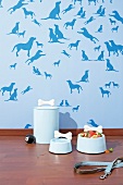 Light blue dog accessories and bowls in front of dog patterned blue wallpaper