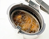 Close-up of chicken meat in deep fryer on white background