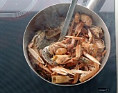 Scampi head, crab legs and other fishes frying in pan with ladle