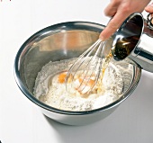 Adding beer to mixture of flour and egg with whisk in bowl, step 1