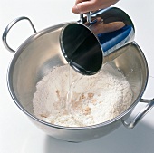 Adding water to flour with yeast in bowl