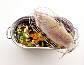 Poached fish on sieve above casserole of vegetable stew