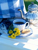 Tee in Tasse in Blau, Butterkeks und Sträußchen Blumen in Gelb, Teekanne