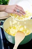 Close-up of woman adding diced vegetables in pot