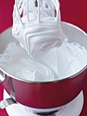 Close-up of meringue whisked with hand mixer in bowl to prepare raspberry pavlova