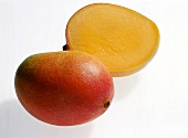 Whole and halved reddish yellow mangoes on white background