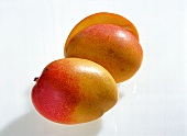 Whole and halved reddish yellow mangoes on white background