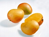 Two whole and halved yellow pear shaped mangoes on white background