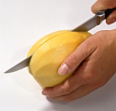 Peeled mango being cut into halves with knife