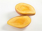 Halved yellow oval shaped mango on white surface
