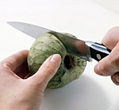 Green custard apple being cut into halves with knife, step 2