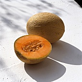 Whole and half cantaloupe melon with orange flesh on white surface