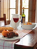 Rotwein im Glas, Karaffe, Weißbrot und Obst auf Tisch am Fenster