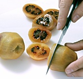 Peeled tamarillo being cut into slices with knife