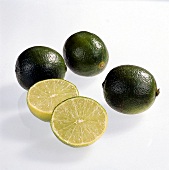 Whole and halved small round green lime on white background
