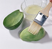 Lemon juice being applied on avocado with brush on white background