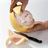 Close-up of hand removing peel of pomelo on white background