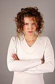 Portrait of angry woman with curly hair wearing white sweater standing with arms crossed