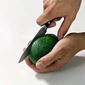 Close-up of hand cutting avocado on white background