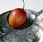 Close-up of tamarillo on slotted spoon above boiling water