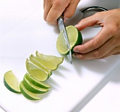 Close-up of hand cutting thin columns of lime on chopping board