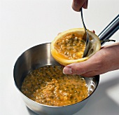Close-up of hand removing pulp from passion fruit in pot