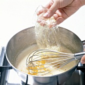 Hand adding gelatine in pot with lemon juice