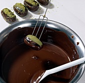 Close-up of stuffed date being dipped in melted chocolate