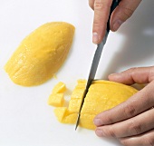 Close-up of hand cutting mango into cubes on white background