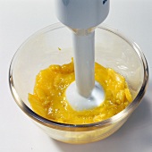 Close-up of hand blending mango pulp with hand blender in bowl