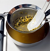 Passion fruit pulp being squeezed with spatula on sieve