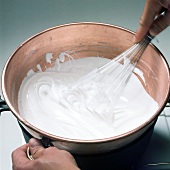 Close-up of hand whisking cream for preparation of decorative meringue, step 1