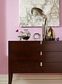 Glossy silver and gold vases on brown dresser against pink wall