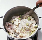 Close-up of vegetables with carcasses in casserole to prepare fish stock, step 3