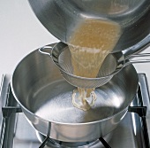Close-up of mixture being passed through sieve in saucepan, step 4
