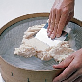 Close-up of hand spreading mixture on sieve, step 5