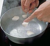 Close-up of hand adding pieces of dumplings in pan with water