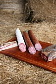 Various sausage and ham on wooden board in hay