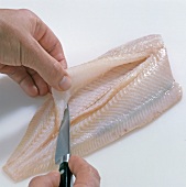 Close-up of hand cutting fish for removing its backbone, step 2