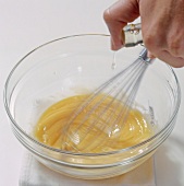 Close-up of hand whisking eggs and adding oil in bowl, step 3, blurred motion