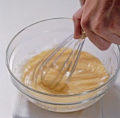 Close-up of hand whisking eggs and adding mustard and oil in bowl, step 4, blurred motion