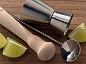 Close-up of jigger, ram, bar spoon and lemon pieces on wooden surface