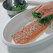 Dill herb being sprinkled on salmon trout, step 2
