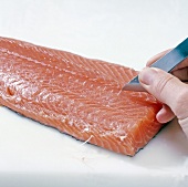 Close-up of hand removing side bones of salmon with tweezers