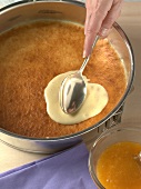 Close-up of hand spreading cream on baked dough for preparing cake. Step 1